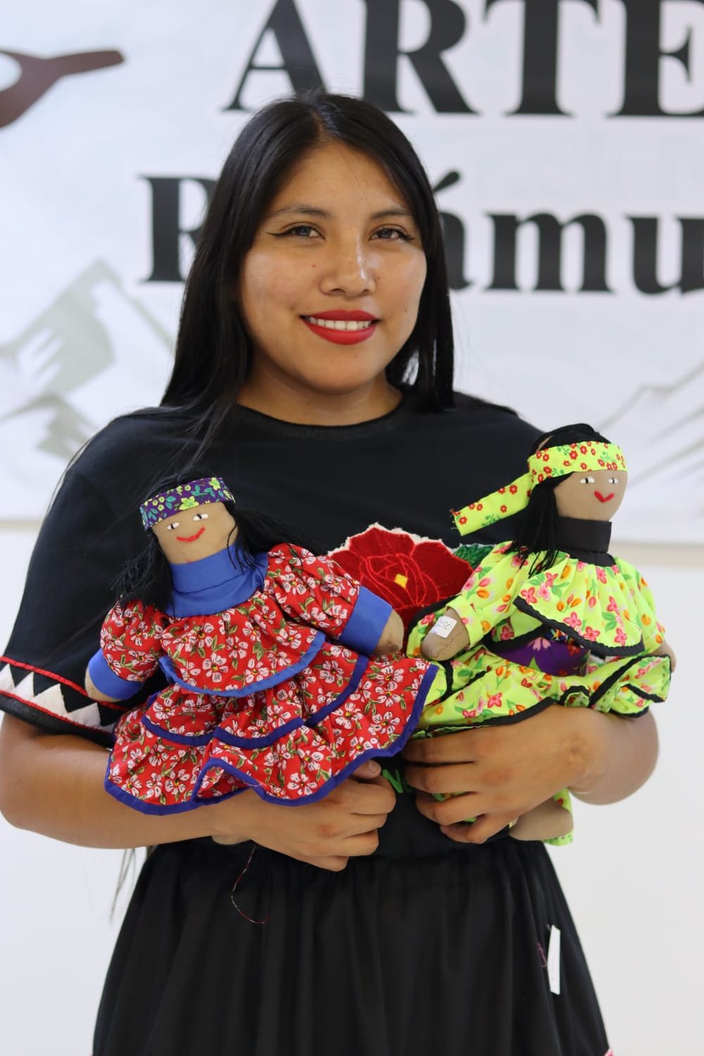 Artesana sosteniendo dos muñecas de tela vestidas con prendas de colores y estampados vivos.