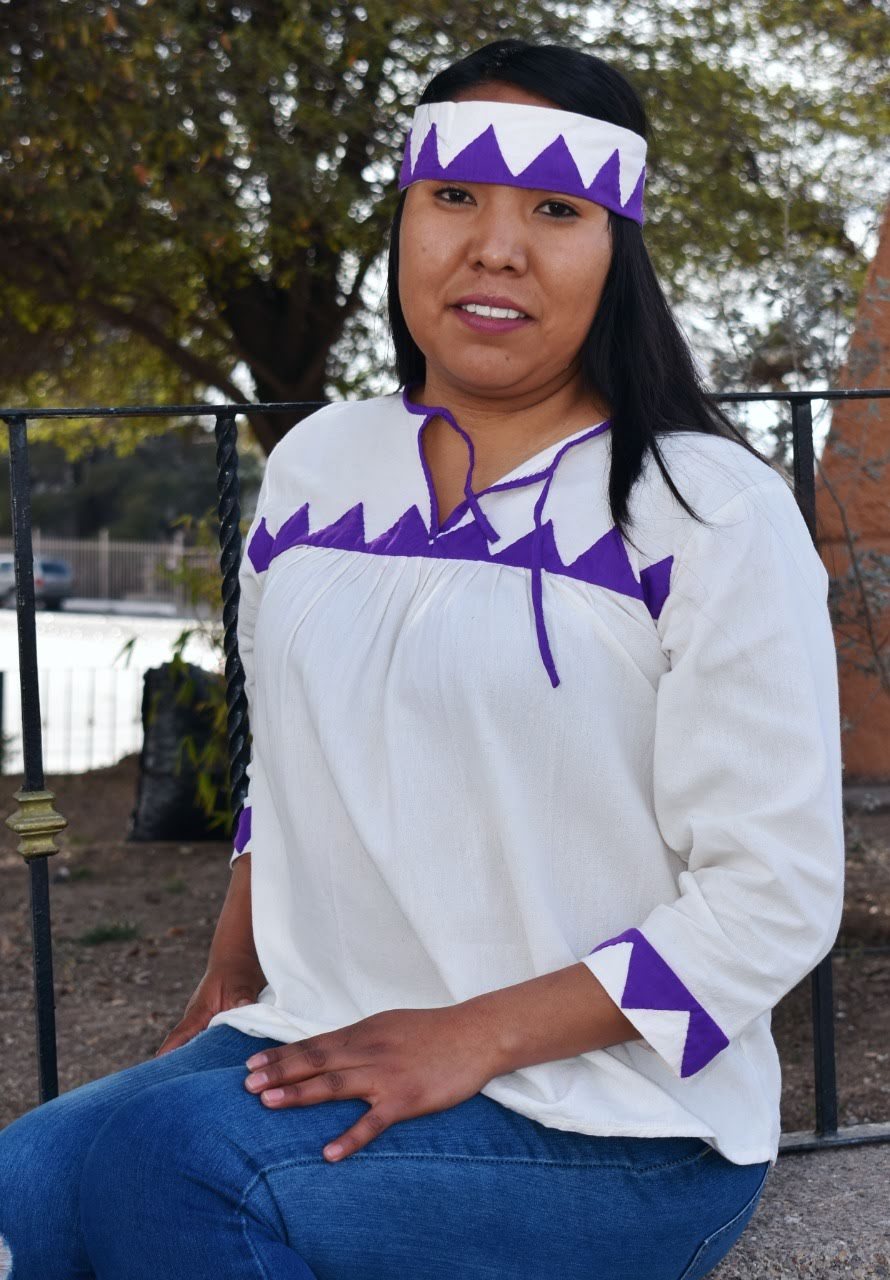 Mujer con blusa blanca, aplicaciones moradas y banda para el cabello a juego.