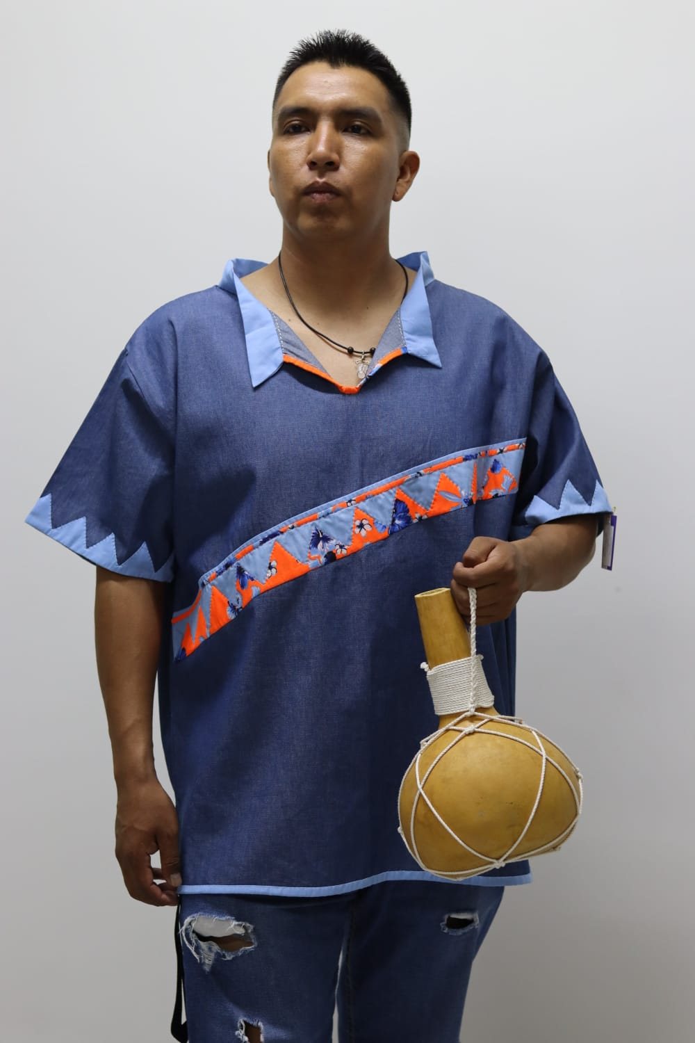 Hombre con camisa azul de cuello abierto y franja geométrica naranja y gris.