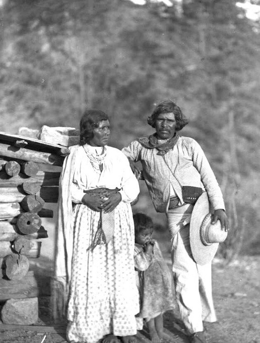 Fotografía histórica en blanco y negro de una familia Ódami del norte junto a una vivienda de madera, vistiendo ropa tradicional en un entorno rural boscoso.
