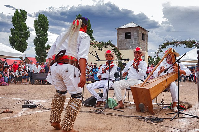 Integrantes de la comunidad Ódami del norte participando en una celebración tradicional con música y danza ceremonial al aire libre.